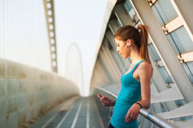 Genç bir kadın müzik dinlerken modern bir köprüde dinleniyor..