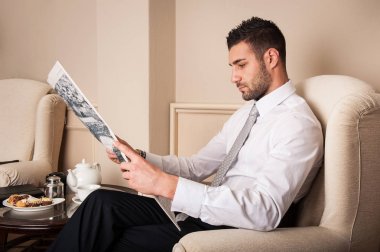 Genç ve rahat iş adamı gazete okuyor. Koltuğa oturuyor..