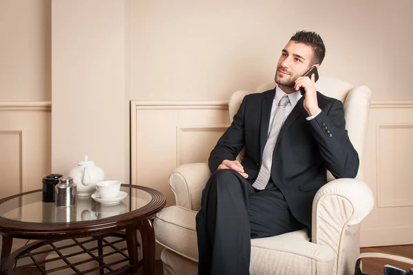 Joven Hombre Negocios Hablando Teléfono Móvil Sentarse Sillón Dentro Hotel —  Fotos de Stock