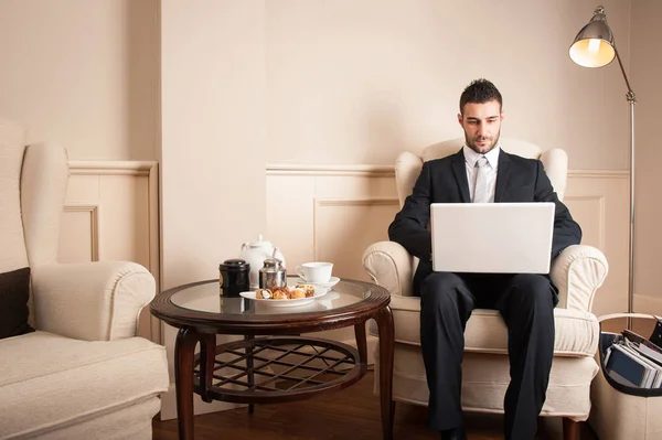 从事便携式计算机工作的年轻商人坐在豪华酒店的扶手椅上 — 图库照片
