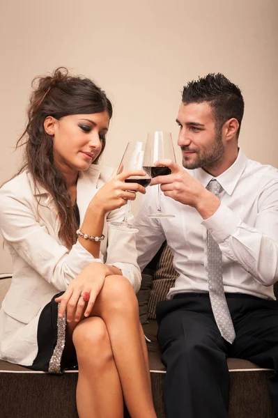 ソファに座ってワイングラスで乾杯するエレガントな若いカップル — ストック写真