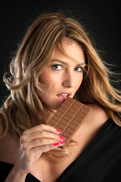 黒い背景にチョコレートバーを持つブロンドの女性 — ストック写真