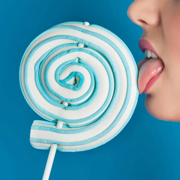 青い背景にロリポップクローズアップ画像を舐める女性 — ストック写真
