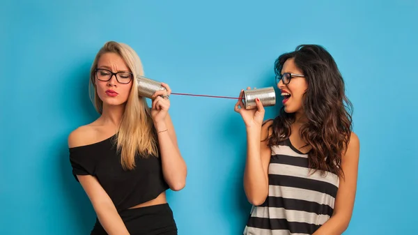 Blonde and brunette women talking with tin can telephone against