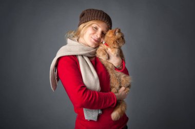 Beautiful woman hugging her red cat portrait on grey background.