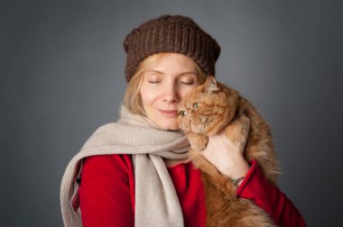 Beautiful woman hugging her red cat portrait on grey background.