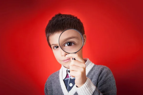 赤を背景に虫眼鏡を通して見る子供 — ストック写真