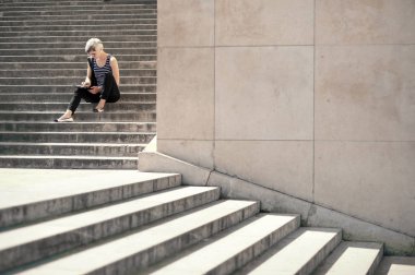 Trocadero 'nun merdivenlerinde otururken tablet kullanan genç sarışın kadın. Paris, Fransa.