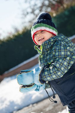 Genç bir çocuk kartopu ile karda eğleniyor..