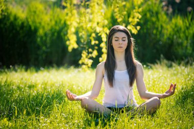 Güzel genç kadın yoga yapıyor, yeşil çim Lotus pozisyonda oturuyor. Sağlıklı yaşam tarzı ve rahatlama kavramı. Filtrelenmiş görüntü.