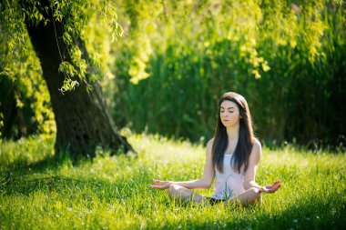 Güzel genç kadın yoga yapıyor, yeşil çim Lotus pozisyonda oturuyor. Sağlıklı yaşam tarzı ve rahatlama kavramı. Filtrelenmiş görüntü.