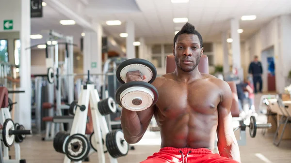 Hombre negro fuerte haciendo ejercicio con pesas en el gimnasio . — Foto de Stock
