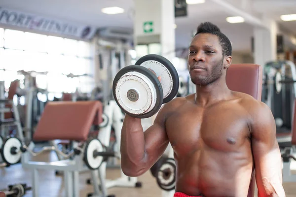 Starker schwarzer Mann beim Training mit Kurzhanteln im Fitnessstudio. — Stockfoto