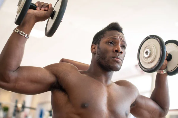 Homme noir fort s'exerçant avec des haltères dans la salle de gym . — Photo