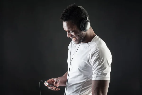 Hombre negro escuchando música con auriculares contra oscuro backgr —  Fotos de Stock