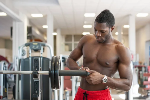 Homme noir fort ajustant la portance lourde sur la barre dans la salle de gym . — Photo