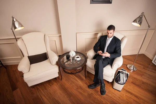 Joven hombre de negocios usando teléfono inteligente sentarse en el sillón interior — Foto de Stock