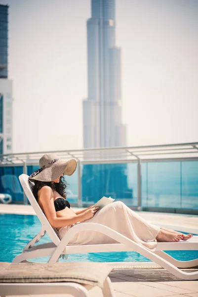 Young woman portrait relaxing and reading a book in swimming pool in Dubai. Filtered image.