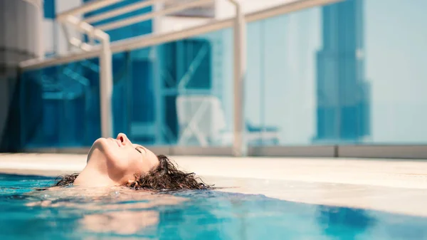 Young woman portrait wearing bikini sunbathing in swimming pool in Dubai. Filtered image.