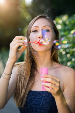 Young woman portrait with soap balloons in a park. Shallow depth of field image with back light and flare effect.