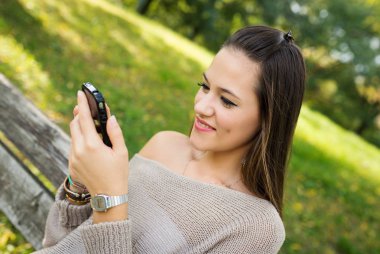 Mutlu genç kadın bir parkta açık havada cep telefonu ile mesaj gönderme. 