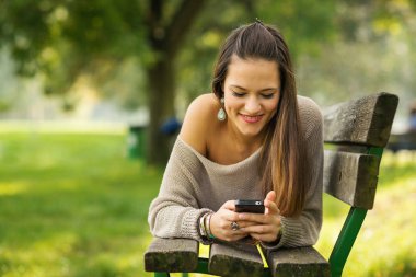 Mutlu genç kadın kopya alanı ile bir parkta cep telefonu ile açık havada mesaj gönderme.