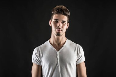 Siyah arka plana karşı beyaz gömlek giyen emin genç adamın portresi. 