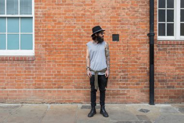 Shoreditch ilçesinde tuğla duvara dayalı genç dövmeli adam portresi. Londra, Uk. Hipster tarzı