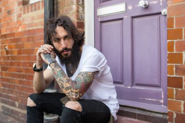 Genç dövmeli adamın yoğun portresi Shoreditch ilçesinde sokakta oturup. Londra, İngiltere. Hipster tarzı