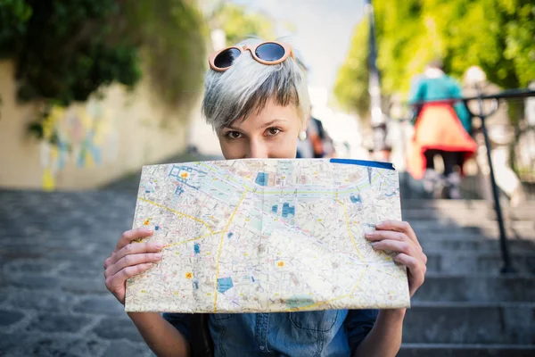 Young blonde woman funny portrait behind map of the city in Montmartre. Paris, France.