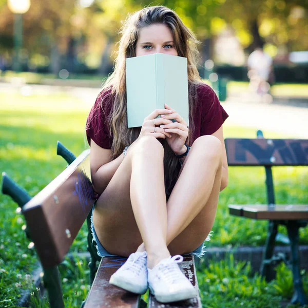 公園の本の後ろに隠れている若い女性 フィルタリングされた画像 — ストック写真