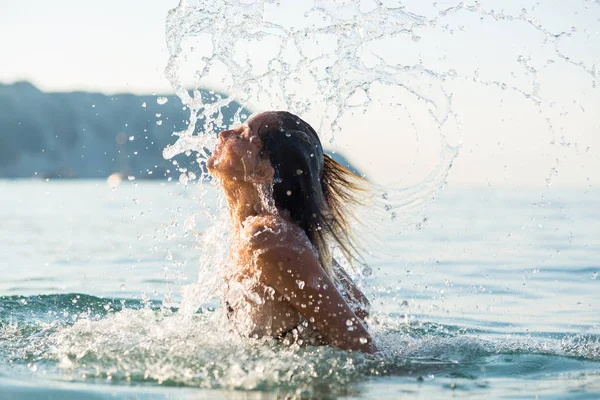 ビーチで水をはねるアクティブな若いブロンドの女性 — ストック写真