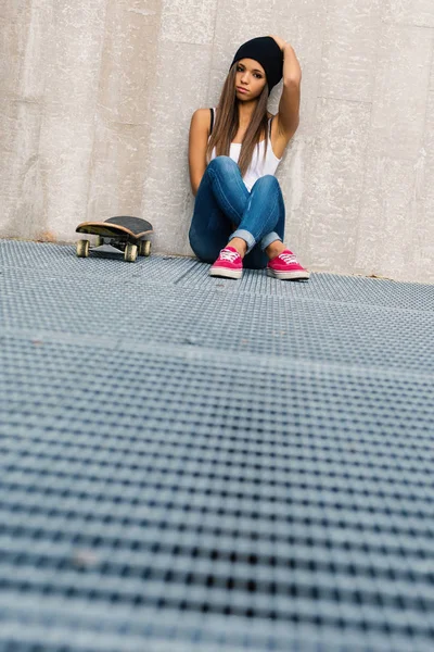 Školní věk se skateboard na portrétu sedí proti betonové stěně. — Stock fotografie