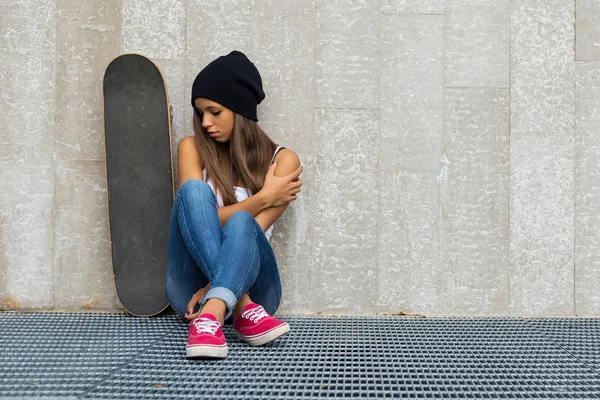 Adolescente com retrato de skate sentar contra parede de concreto . — Fotografia de Stock