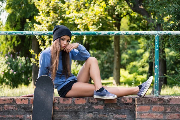 Retrato adolescente con monopatín sentarse en la pared de ladrillo al aire libre en —  Fotos de Stock