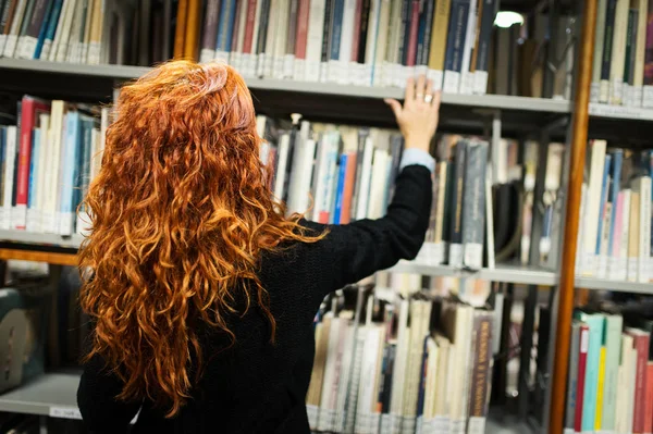 Jovem estudante do sexo feminino livro de consultoria de prateleira em biblioteca pública — Fotografia de Stock