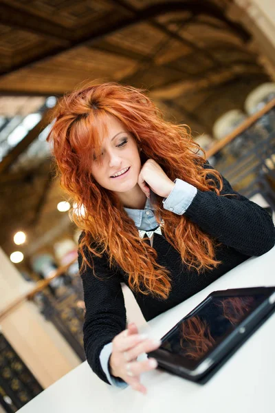 Junge rothaarige Frau mit Tablet in öffentlicher Bibliothek. — Stockfoto