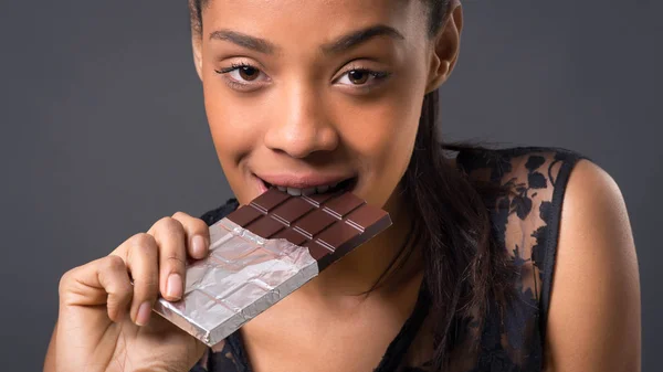 暗い背景にチョコレートバーを食べる官能的なブルネットブラジルの女性 — ストック写真