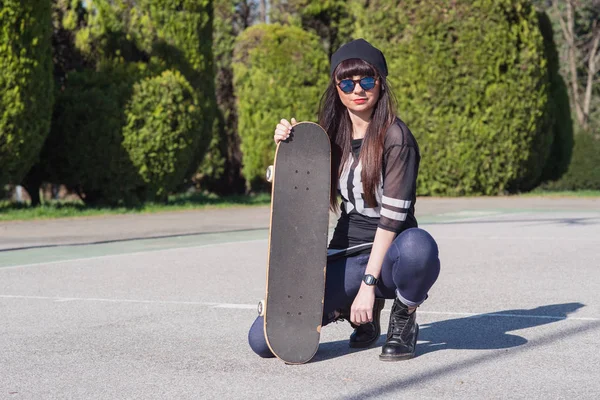 Young woman with skateboard outdoors in a basketball playground.