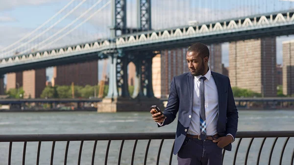 Joven hombre de negocios usando teléfono móvil con Manhattan Bridge —  Fotos de Stock