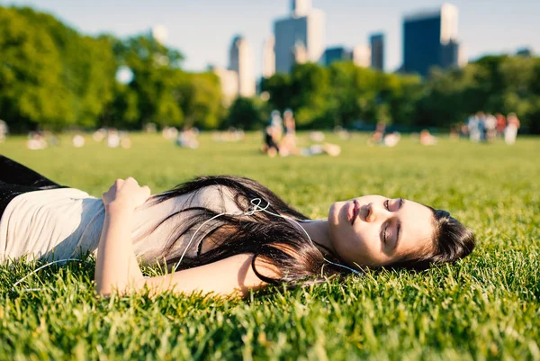 年轻女子在中央公园休息 躺在草地上听音乐 过滤图像 — 图库照片