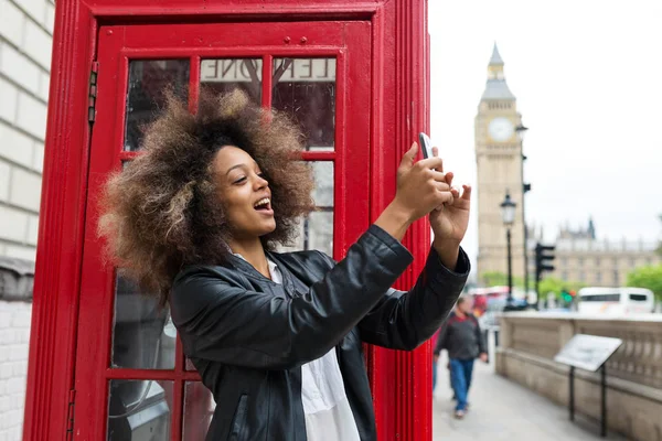 Młoda kobieta portret blisko czerwonej budki telefonicznej w Londynie biorąc — Zdjęcie stockowe