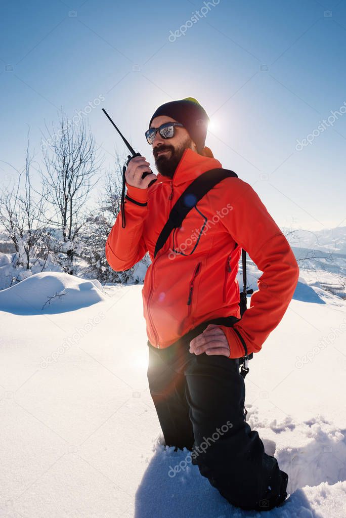 Rescue man talking with portable radio on mountain snow landscape. Back light image.