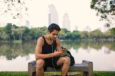 Lumpini Park, Bangkok açık egzersiz sonra şehir parkı içinde akıllı telefon kullanarak Adam.