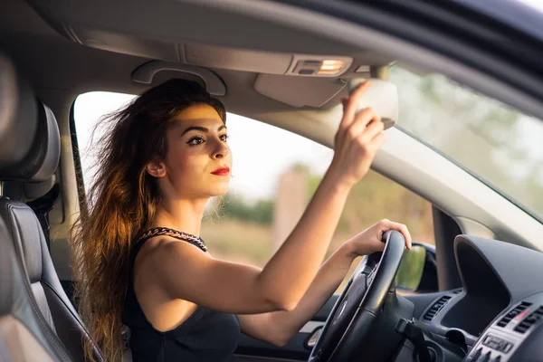 Woman portrait sit in her car looking at the mirror checking make up. Filtered image.