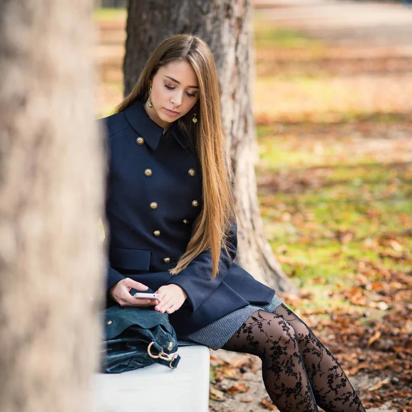 Молода блондинка на відкритому повітрі в парку восени надсилає повідомлення — стокове фото