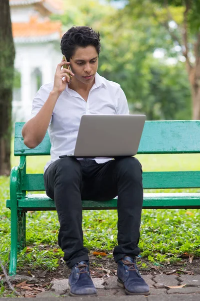 Jovem Homem Bonito Trabalhando Com Laptop Falando Telefone Enquanto Sentado — Fotografia de Stock