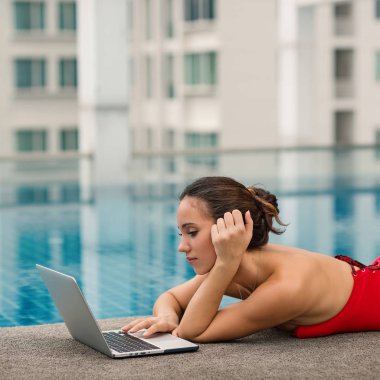 Bangkok, Tayland 'da yüzme havuzunda laptopuyla çalışan kırmızı mayo giyen bir kadın..