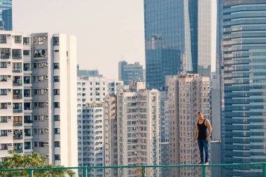 Portrait of parkour man walking on fence with Hong Kong skyline in the background.