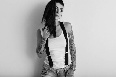 Dövmeli kadın portresi ve beyaz duvara asılı pantolon askısı. Bl